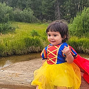 Allyson is registered to the contest to win money with this photo: child, toddler, costume, dress, yellow_tutu, black_shoes, outdoor, nature, greenery, wooden_fence, creek, grass, smiling, happy, portrait, cute, fashion, person, playful, scenery