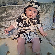 Teddie is registered to the contest to win money with this photo: baby, child, clothing, couch, curious, cushion, expression, face, footwear, hand, hat, indoor, infant, legs, looking_up, patterned_outfit, person, plush_furniture, sitting, young
