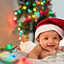 baby, smiling, santa_hat, christmas_lights, christmas_tree, holiday, festive, infant, blanket, cute, happy, indoors, decorations, portrait, child, celebration, colorful, warm, holiday_spirit, tongue_out