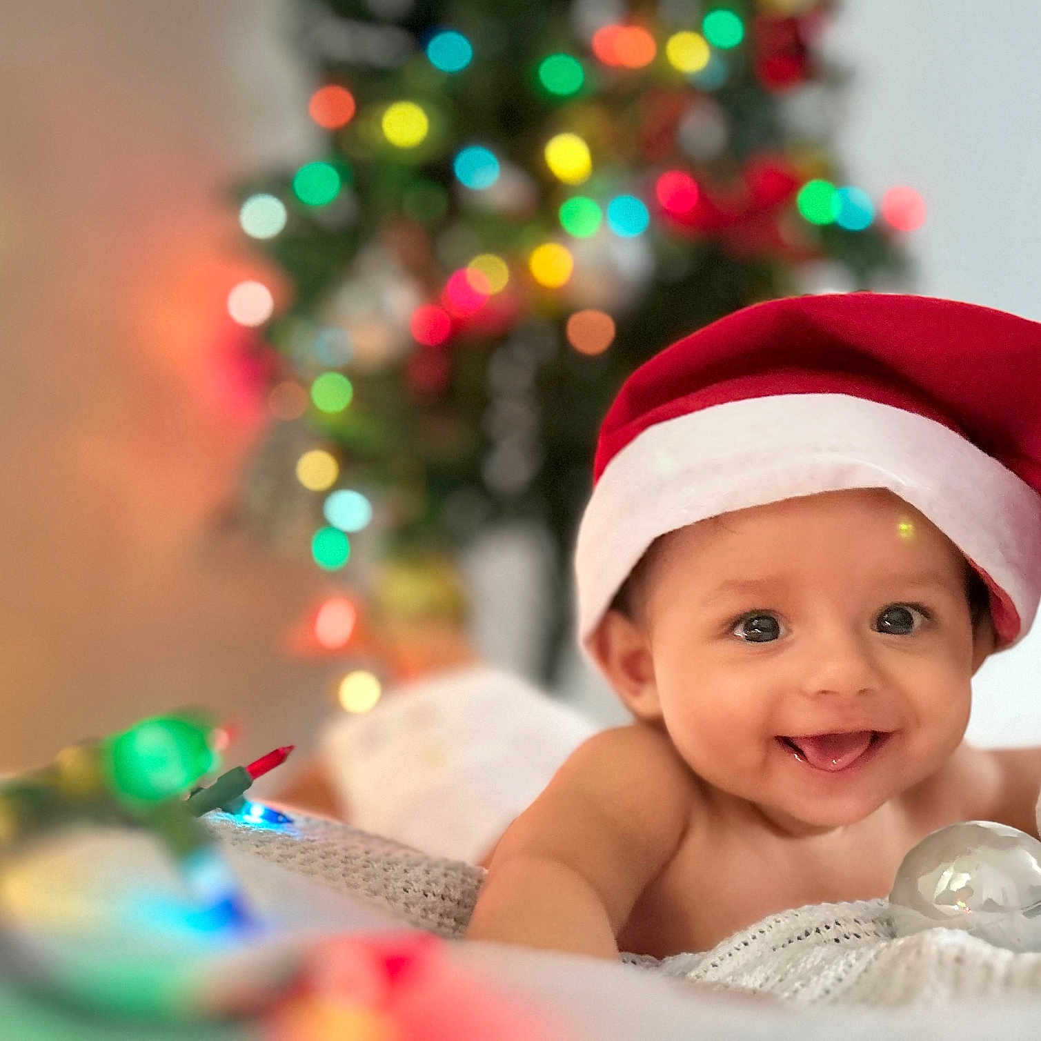 Shriyan Rakshit joined the competition — help win amazing prizes! baby, blanket, celebration, child, christmas_lights, christmas_tree, colorful, cute, decorations, festive, happy, holiday, holiday_spirit, indoors, infant, portrait, santa_hat, smiling, tongue_out, warm