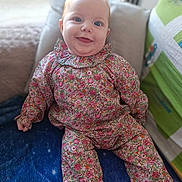 Adèlia a rejoint le concours — aidez-le/la à gagner de superbes lots ! baby, child, smiling, blue_eyes, floral_outfit, blanket, couch, indoor, cozy, cute, happy, portrait, sitting, infant, clothing, colorful, soft_light, home, pillow, cheerful