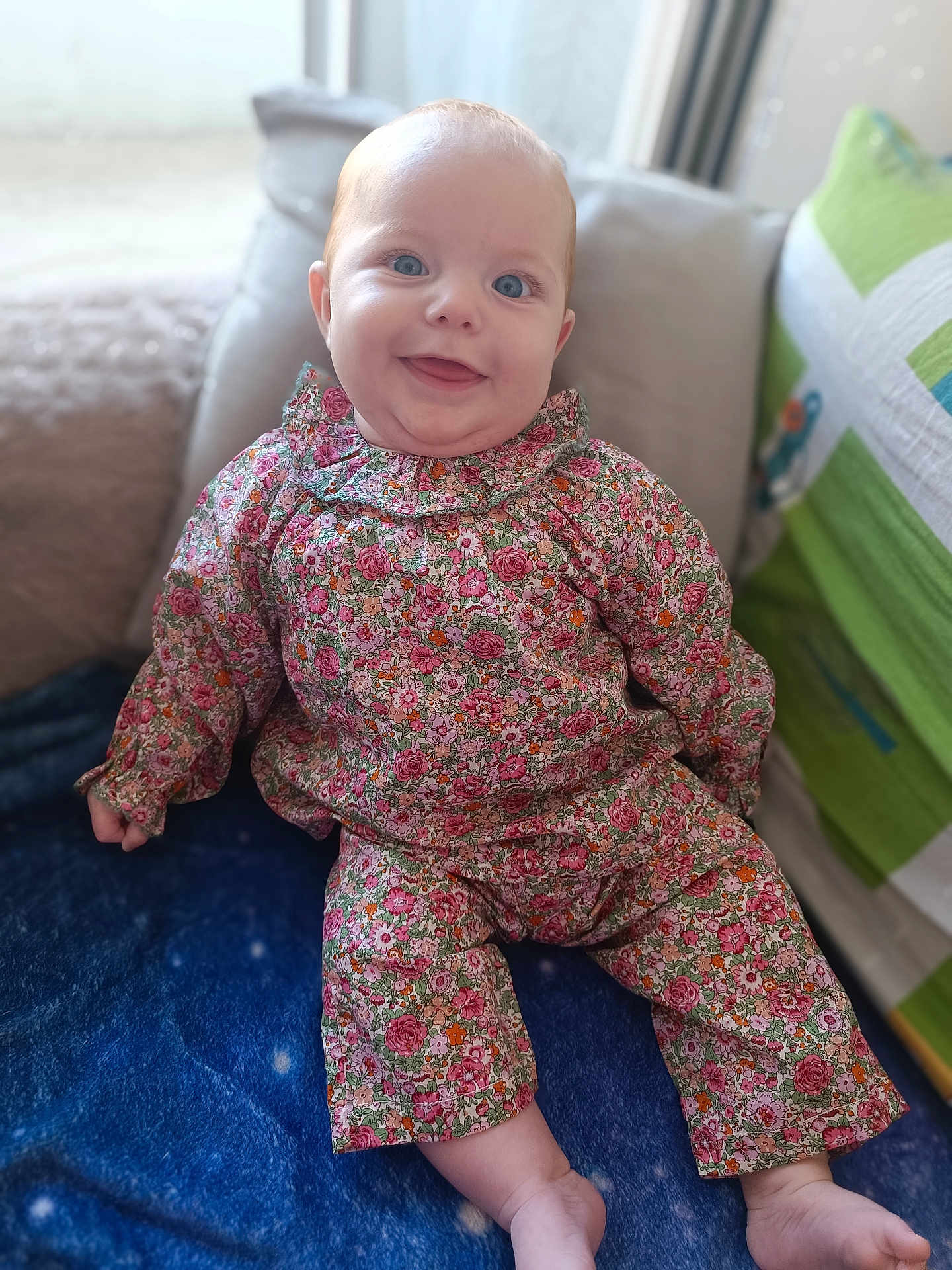 Adèlia a rejoint le concours — aidez-le/la à gagner de superbes lots ! baby, child, smiling, blue_eyes, floral_outfit, blanket, couch, indoor, cozy, cute, happy, portrait, sitting, infant, clothing, colorful, soft_light, home, pillow, cheerful