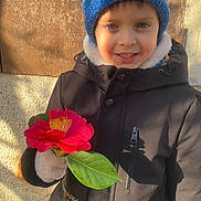David Mihai participe au concours pour gagner de l'argent avec cette photo : child, smiling, flower, red_flower, blue_hat, winter_coat, gloves, outdoor, sunlight, shadow, wall, leaf, portrait, young_child, happy, nature, seasonal, casual_clothing, person, daylight