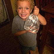 Nicholas joined the competition — help win amazing prizes! child, boy, curly_hair, smiling, indoor, wooden_floor, plastic_bag, fish, water, holding, casual_clothing, shorts, shoes, happy, portrait, young, person, home, furniture, light