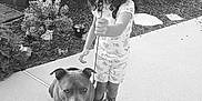 Kaya is registered to the contest to win money with this photo: child, dog, outdoor, sidewalk, garden, plant, slide, toy, pinwheel, black_and_white, curly_hair, rain_boots, leash, smile, playful, pet, nature, young_girl, animal, portrait