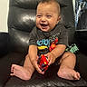 baby, child, smiling, toy_car, black_chair, leather_chair, sitting, happy, indoor, cute, short_hair, barefoot, clothing, playful, infant, person, portrait, furniture, background, mohawk