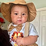 baby, child, hat, bow_tie, shirt, lion_print, suspenders, indoor, face, portrait, cute, chubby_cheeks, expression, person, infant, clothing, light, skin, hand, background