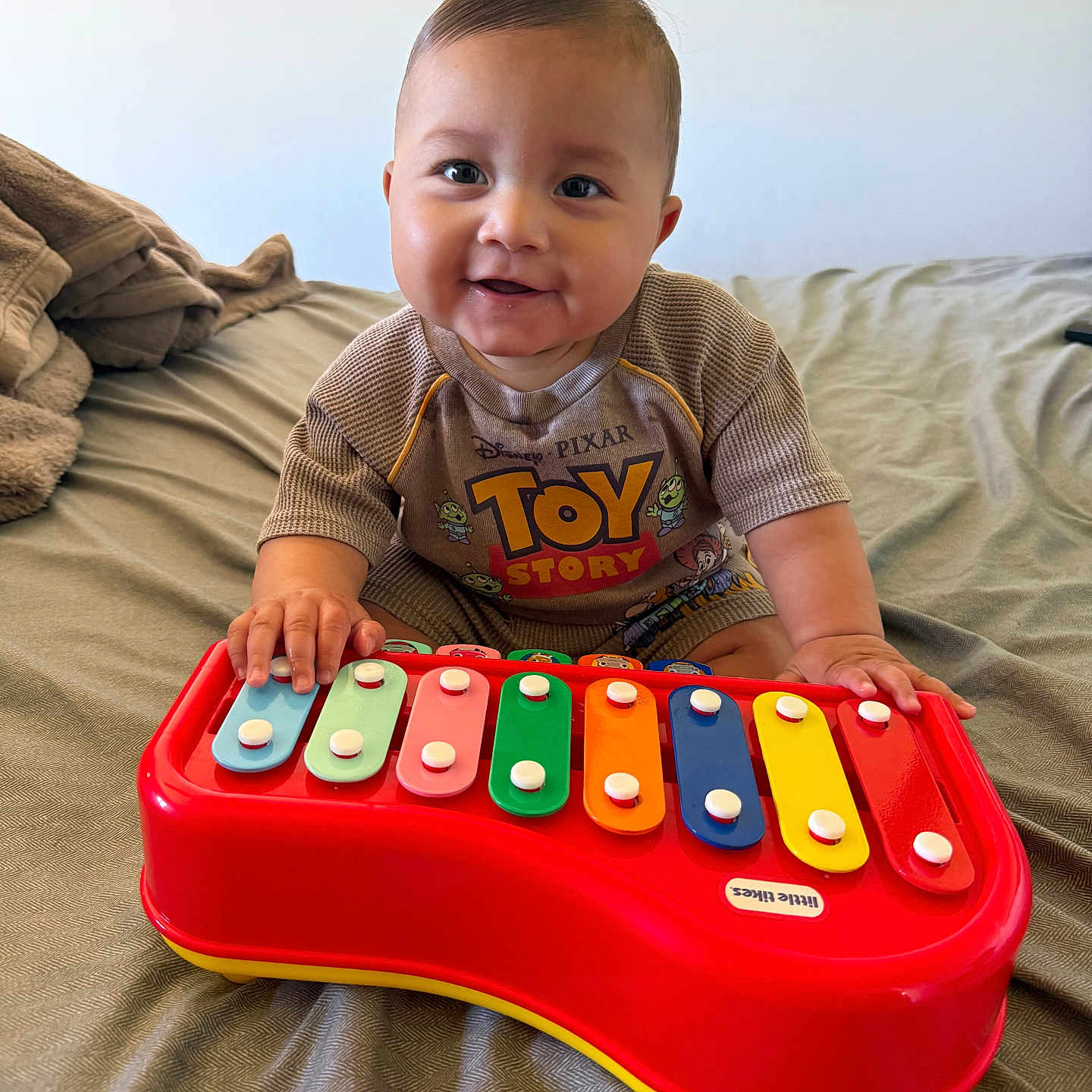 Andres joined the competition — help win amazing prizes! baby, child, toy_story, xylophone, toy, bed, smile, happy, indoors, clothing, colorful, play, cute, person, infant, music, hand, face, young, sitting