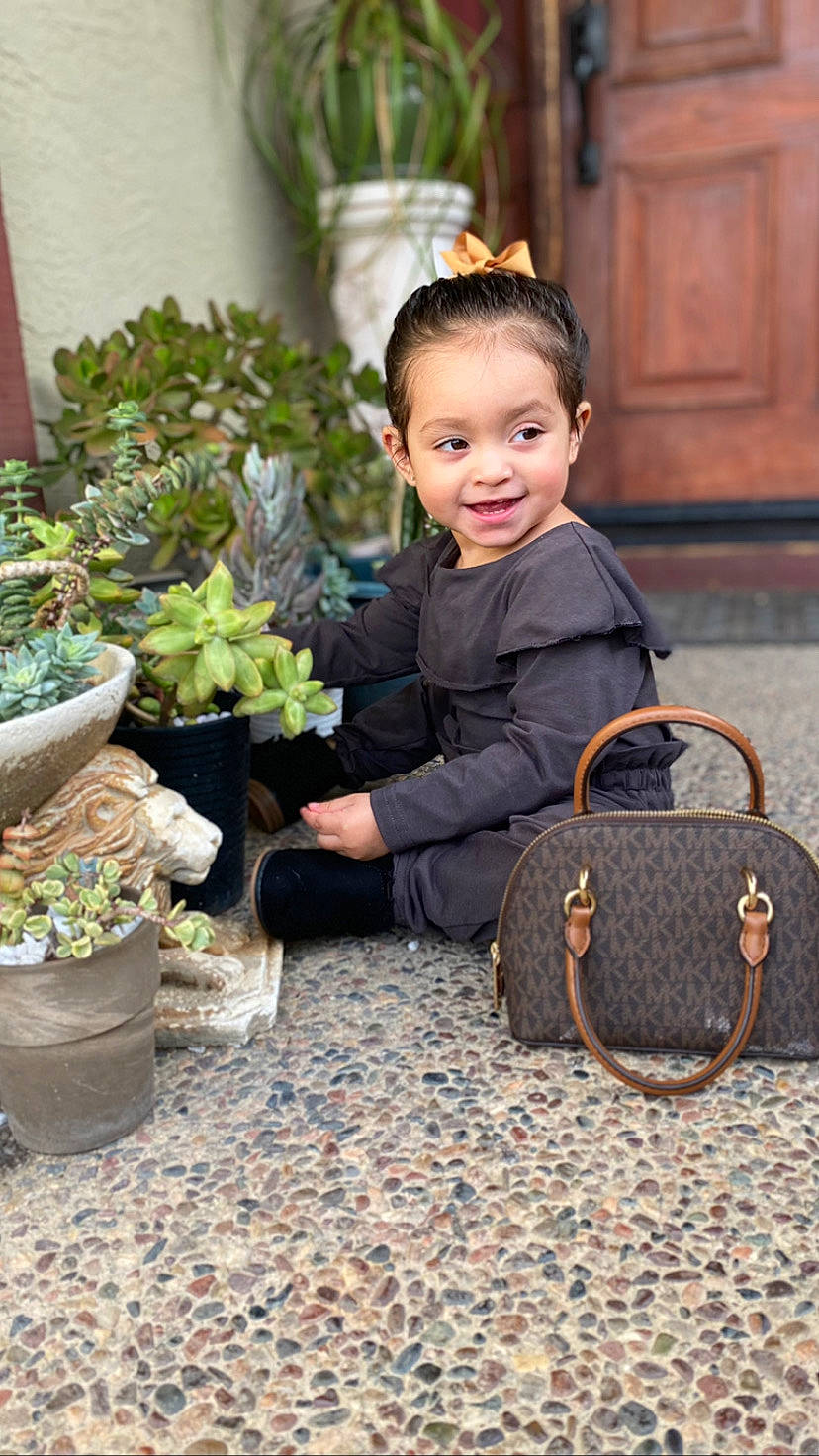 Ximena is registered to the contest to win money with this photo: annual_plant, child, dress, flooring, flower, flowerpot, formal_wear, grass, happy, herb, houseplant, joy, leisure, luggage_and_bags, person, plant, shrub, sitting, sleeve, smile