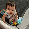 toddler, child, baby, toys, plush_toy, playpen, carpet, indoor, curious, looking_up, colorful, soft, mesh, clothing, person, cute, young_child, infant, smiling, holding