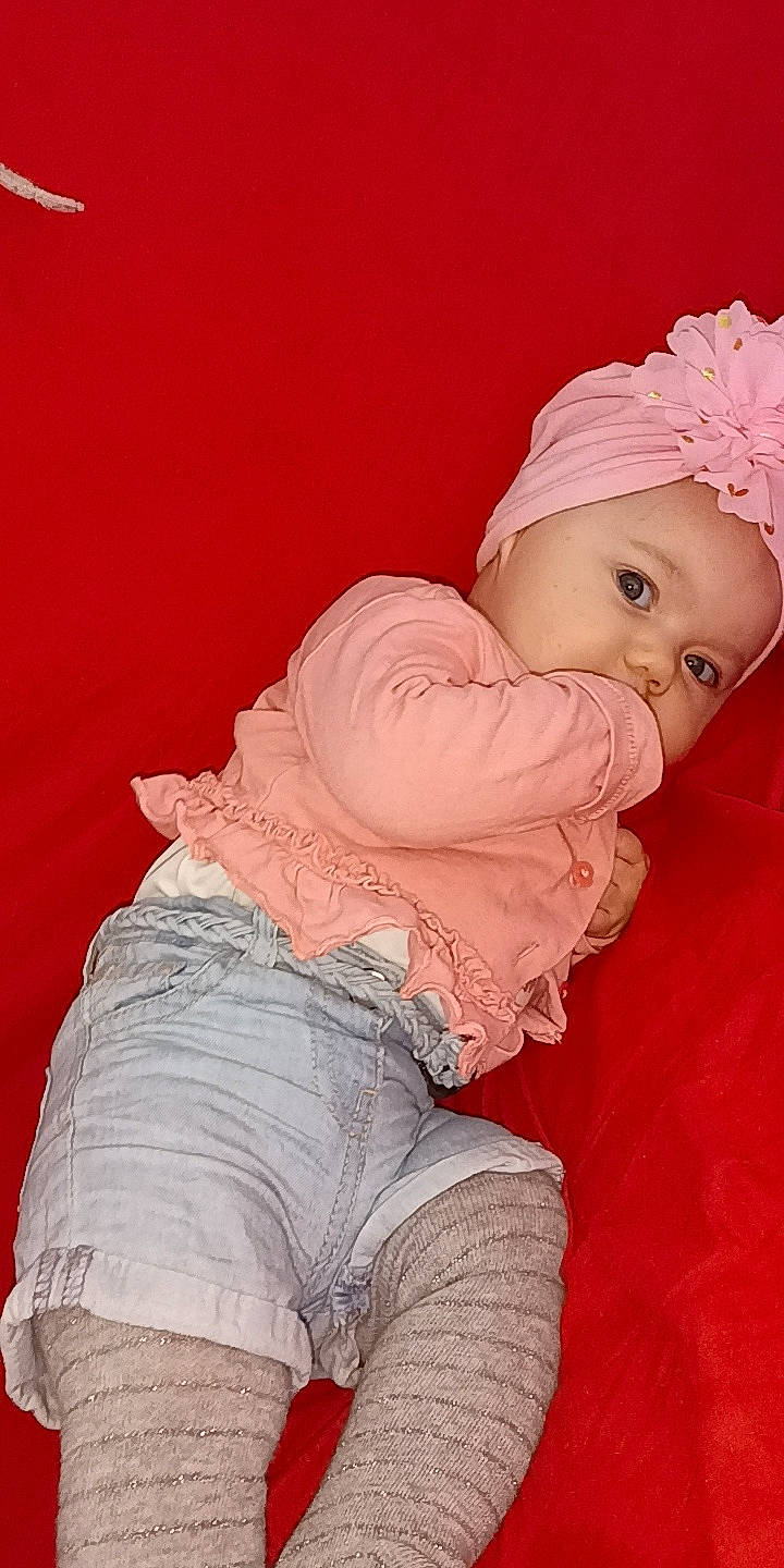 Kenza participe au concours pour gagner de l'argent avec cette photo : abdomen, baby, baby_toddler_clothing, cap, cheek, child, comfort, hat, headwear, human_body, human_leg, knee, magenta, pattern, peach, person, pink, shorts, sitting, sleeve