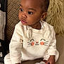 toddler, child, baby, indoors, couch, sneakers, white_shoes, cute_outfit, long_sleeves, plush_texture, earrings, curly_hair, seated, cozy, cushions, soft_lighting, portrait, expression, curious, home
