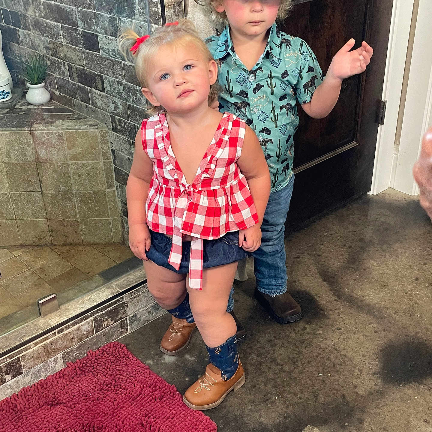 Stevie Gray Dean joined the competition — help win amazing prizes! bathroom, blue_shorts, boots, child, concrete_floor, cowboy_hat, curious_expression, curly_hair, door, indoor, jeans, person, pigtails, red_bow, red_checkered_top, rug, shirt, standing, tile_wall, toddler