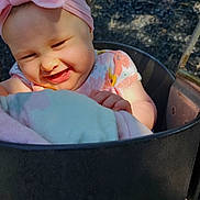 Hazel is registered to the contest to win money with this photo: baby, child, infant, smiling, laughing, face, portrait, pink_bow, headband, floral_clothing, stroller, outdoor, sunlight, seated, blanket, happy, close_up, baby_carriage, black_tray, playful