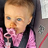 Hazel is registered to the contest to win money with this photo: baby, infant, child, car_seat, safety_harness, pacifier, pink_clothing, sweater, blue_eyes, brown_hair, sitting, portrait, indoors, vehicle, headrest, seatbelt, floral_strap, close_up, alert, safe