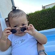 Ariah a rejoint le concours — aidez-le/la à gagner de superbes lots ! toddler, child, sunglasses, white_shirt, elephant_print, hair_buns, outdoor, pool, hedge, adult_arm, watch, bracelet, curious, summer, sunny, baby, striped_pants, person, holding, portrait