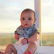 Liam is registered to the contest to win money with this photo: baby, child, infant, window, natural_light, curious, sitting, clothing, shorts, bracelet, indoors, portrait, cute, face, skin, toes, background, scenery, daylight, expression