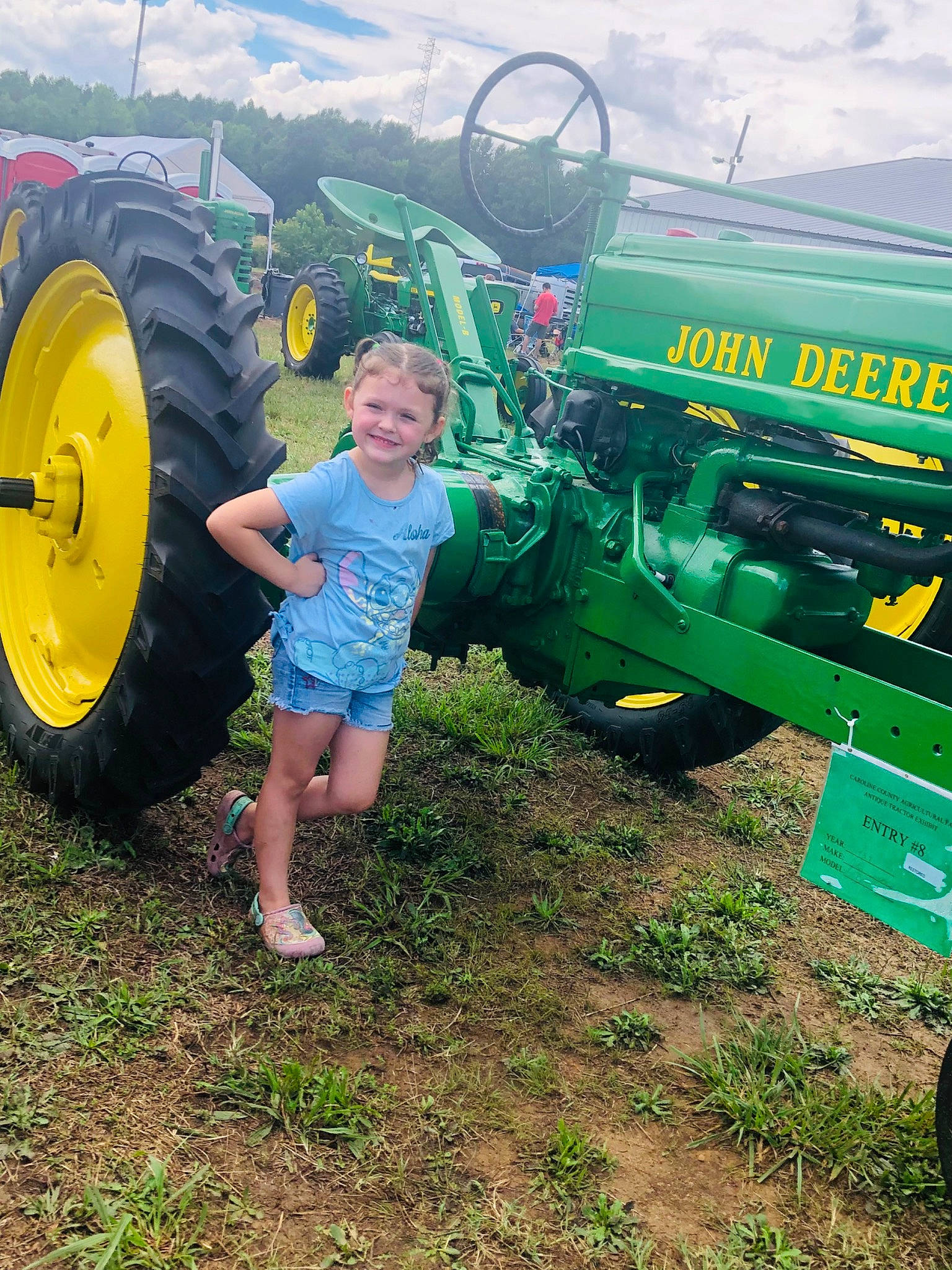 Madilynn joined the competition — help win amazing prizes! agricultural_machinery, agriculture, automotive_tire, cloud, farmer, farmworker, fender, grass, grassland, green, joy, motor_vehicle, person, plant, rural_area, shorts, smile, tire, tractor, tread