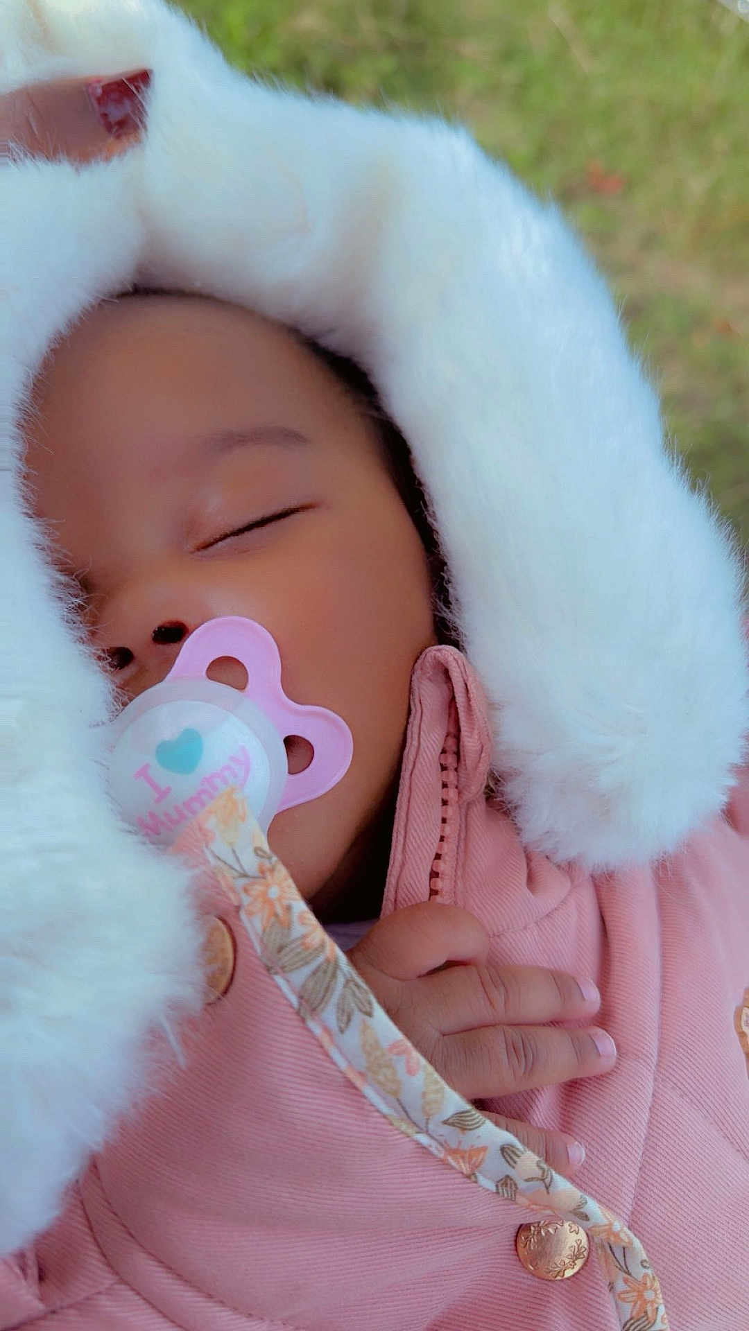 Malya a rejoint le concours — aidez-le/la à gagner de superbes lots ! baby, sleeping, pacifier, pink_jacket, fluffy_hood, hand, red_nail_polish, close_up, outdoor, green_background, peaceful, child, infant, cozy, cute, portrait, warm_clothing, toddler, face, soft