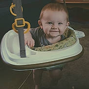 Jaxson joined the competition — help win amazing prizes! baby, smiling, indoor, baby_jumper, child, face, toy, carpet, furniture, table, red_cup, happy, person, clothing, living_room, floor, seat, play, cute, infant
