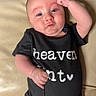 Braxton is registered to the contest to win money with this photo: baby, infant, onesie, black_clothing, couch, furniture, raised_fist, pose, face, skin, head, blue_eyes, expression, comfort, indoor, text_on_clothing, blanket, towel, person, newborn