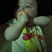 Braxton is registered to the contest to win money with this photo: baby, infant, pacifier, onesie, winnie_the_pooh, tigger, cartoon, child, cute, portrait, sleepwear, hand, face, blue_eyes, soft_lighting, dark_background, person, lying_down, baby_clothes, infant_toys