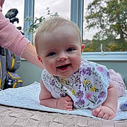 Lillie is registered to the contest to win money with this photo: baby, smiling, bib, blanket, window, indoor, child, person, happy, face, arm, hand, clothing, plant, nature, tree, light, curious, couch, support