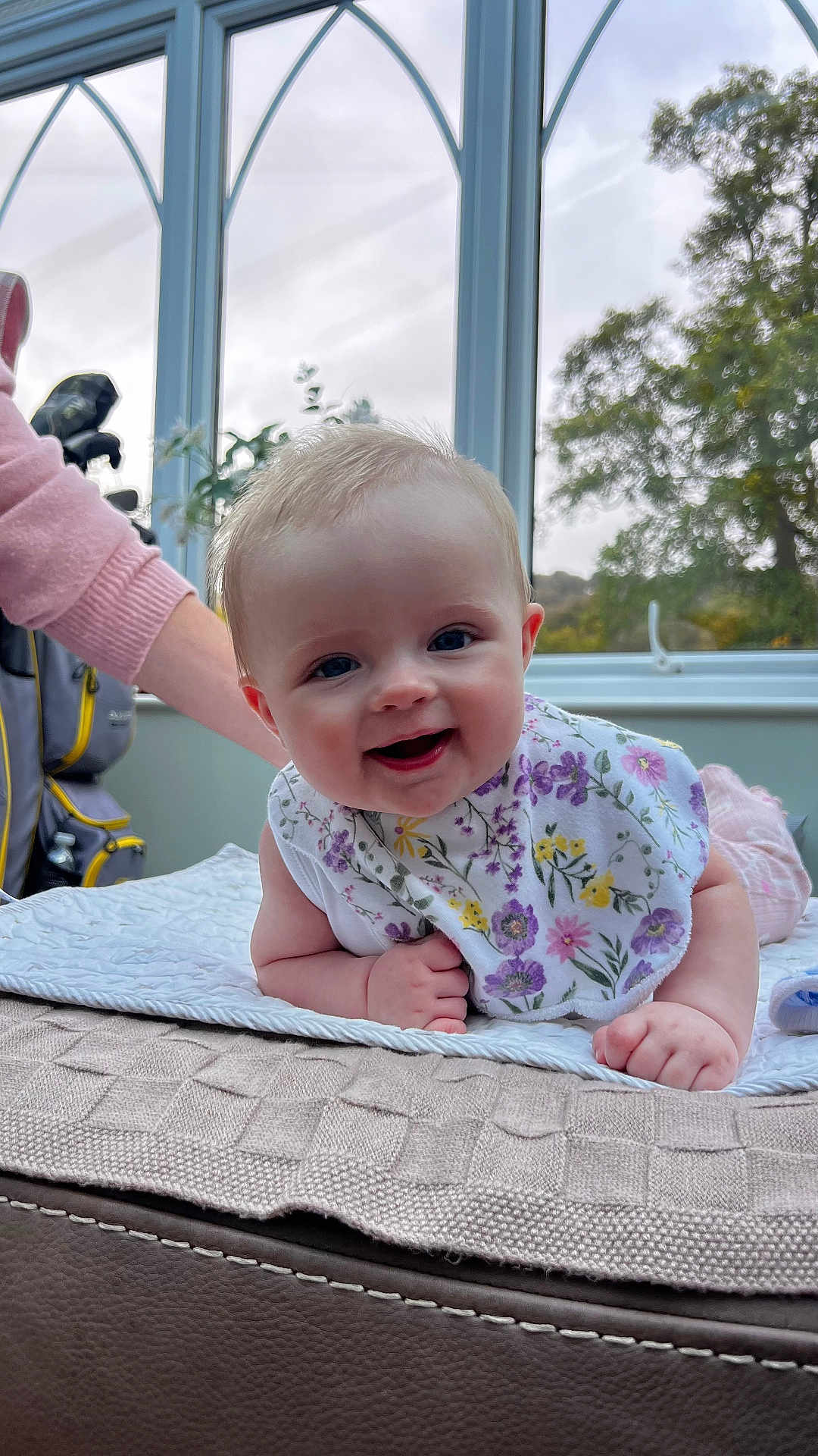 Lillie is registered to the contest to win money with this photo: baby, smiling, bib, blanket, window, indoor, child, person, happy, face, arm, hand, clothing, plant, nature, tree, light, curious, couch, support