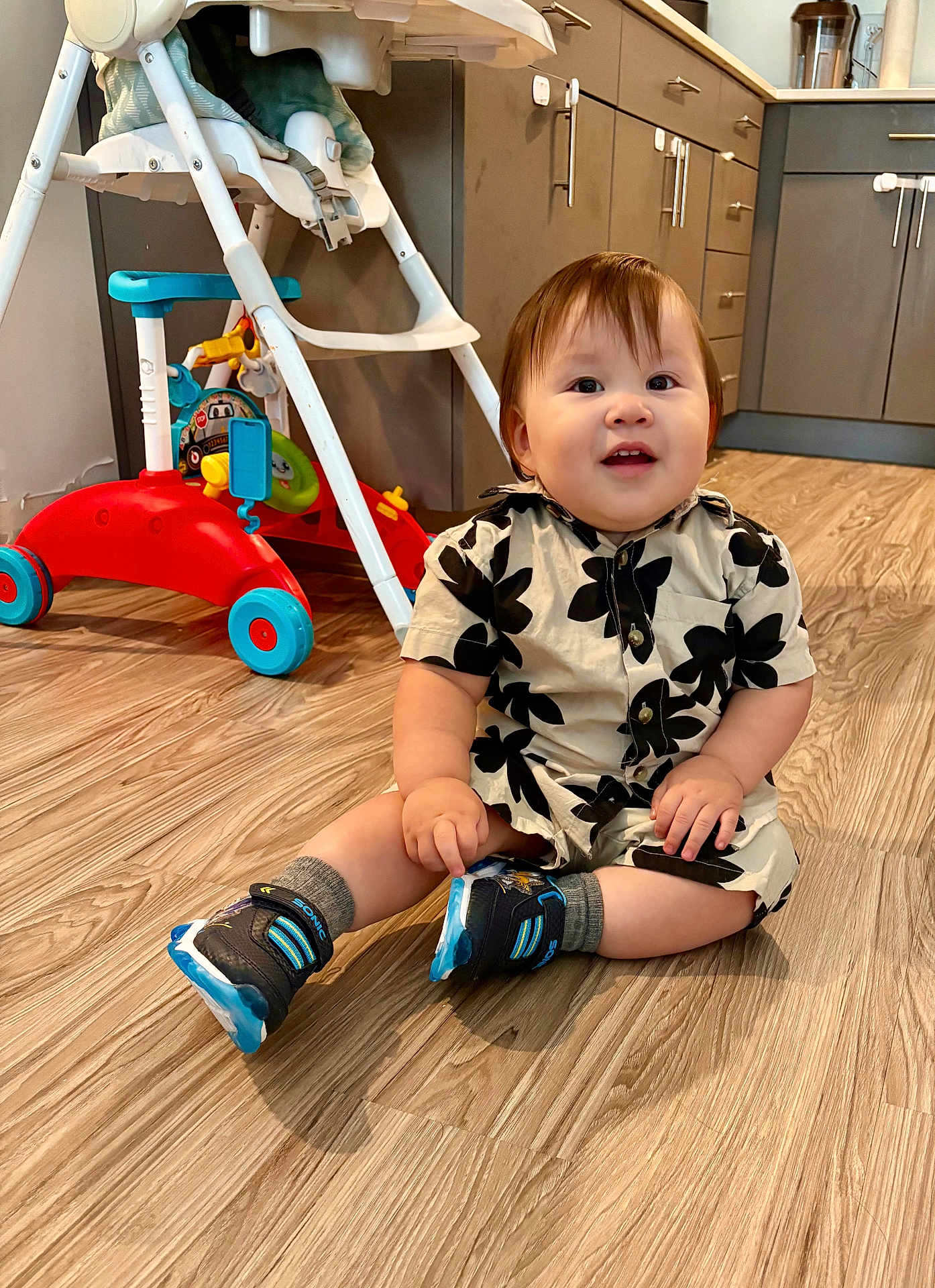 Gabriel García joined the competition — help win amazing prizes! baby, child, sitting, floor, kitchen, wooden_floor, shoes, clothing, toy, walker, smiling, indoor, person, shorts, cabinet, drawer, happy, cute, infant, home