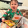 toddler, child, book, reading, pajamas, bed, blanket, smile, happy, indoors, striped_pants, santa_claus, face, foot, hair, furniture, person, cozy, playful, colorful