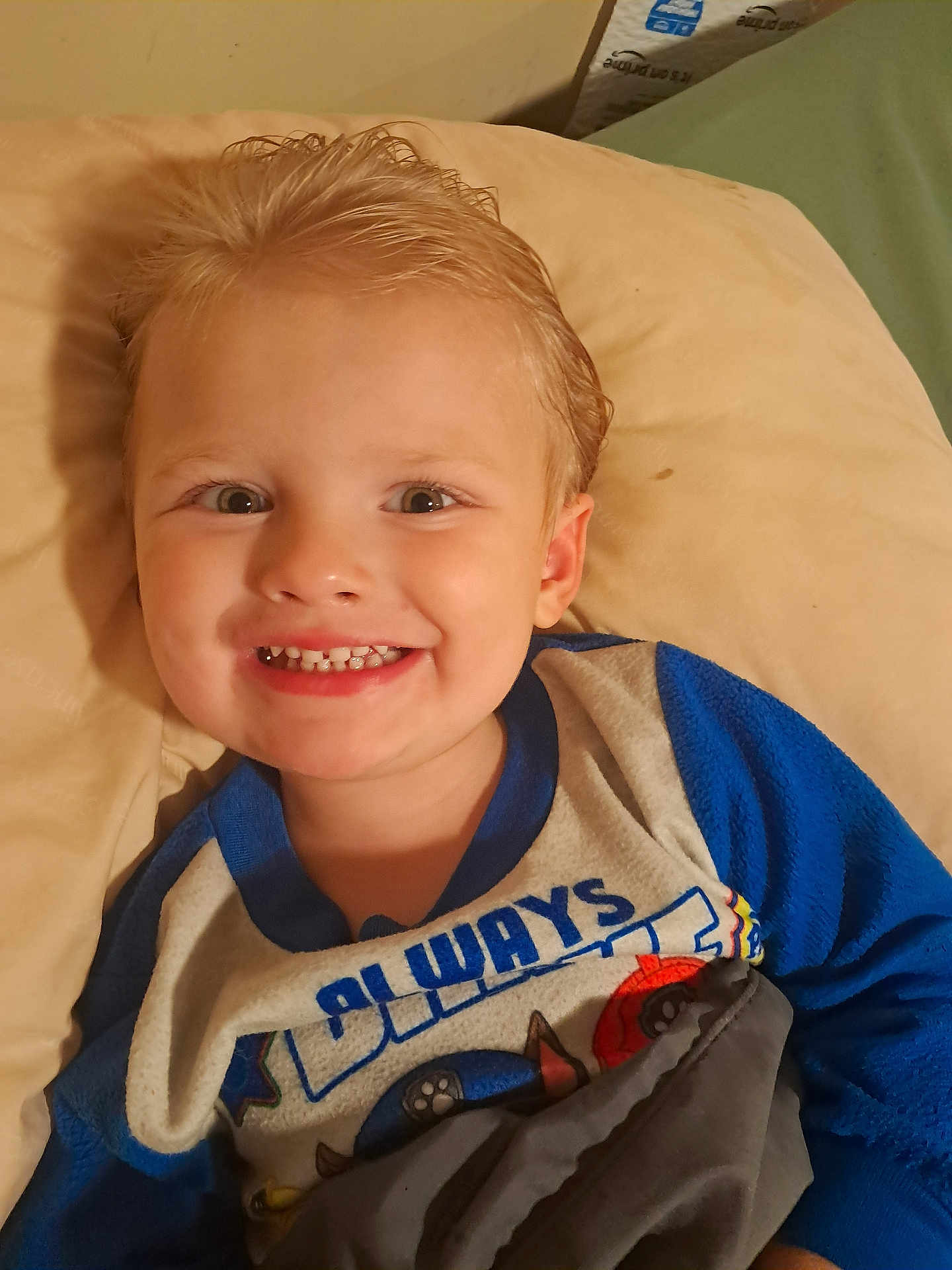 Kobe is registered to the contest to win money with this photo: child, toddler, smile, face, blond_hair, pajamas, blanket, pillow, indoor, happy, cute, portrait, young_child, bedroom, cozy, person, clothing, resting, lying_down, closeup