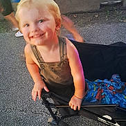 Kobe is registered to the contest to win money with this photo: toddler, child, blonde_hair, smiling, stroller, blanket, pavement, outdoor, people, concrete, wheel, hand, clothing, person, daylight, blur, happy, young_child, casual, playful