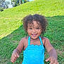 child, toddler, curly_hair, blue_swimsuit, grass, outdoor, smiling, happy, summer, sunny, nature, playful, person, young_child, greenery, daylight, cute, portrait, fun, casual