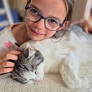Maëlys a rejoint le concours — aidez-le/la à gagner de superbes lots ! child, glasses, cat, petting, sleeping_cat, tablecloth, indoor, portrait, face, smile, hand, animal, young, person, cozy, closeup, furniture, cute, affection, resting