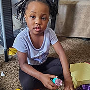 Ava joined the competition — help win amazing prizes! child, toy, carpet, pigtails, indoor, curious, play, tshirt, black_pants, hand, face, person, floor, plastic_toy, young_child, home, candid, sitting, concentration, casual