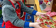 Killian joined the competition — help win amazing prizes! child, toy, pizza, red_hat, red_apron, play_kitchen, carpet, colorful, indoor, pretend_play, hoodie, sneakers, wooden_furniture, cup, oven_mitt, learning_environment, preschool, playroom, young_child, imaginative_play