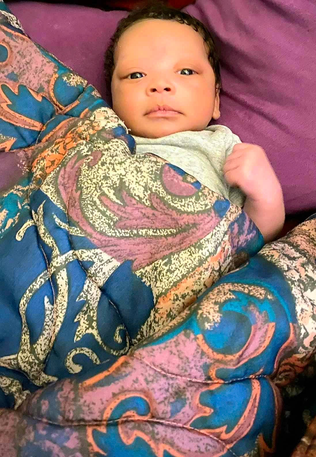 Legend is registered to the contest to win money with this photo: art, baby, beauty, cheek, chest, close_up, comfort, hairstyle, happy, iris, linens, neck, pattern, person, sitting, skin, sleeve, textile, toddler, trunk