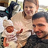 newborn, baby, child, family, father, sibling, portrait, selfie, smiling, sleeping, indoors, bedroom, hotel_room, window, cityscape, baby_hat, onesie, blanket, necklace, family_photo