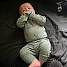 baby, infant, child, lying_down, bed, blanket, dark_background, green_outfit, mitten, mittens, clothing, plush_toy, stuffed_animal, face, portrait, indoor, cozy, relaxed, feet, photography