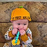 baby, child, infant, halloween, costume, orange_hat, couch, sitting, toy, teething, pacifier, smiling, portrait, indoors, baby_clothing, patterned_outfit, orange, colorful, face, safe