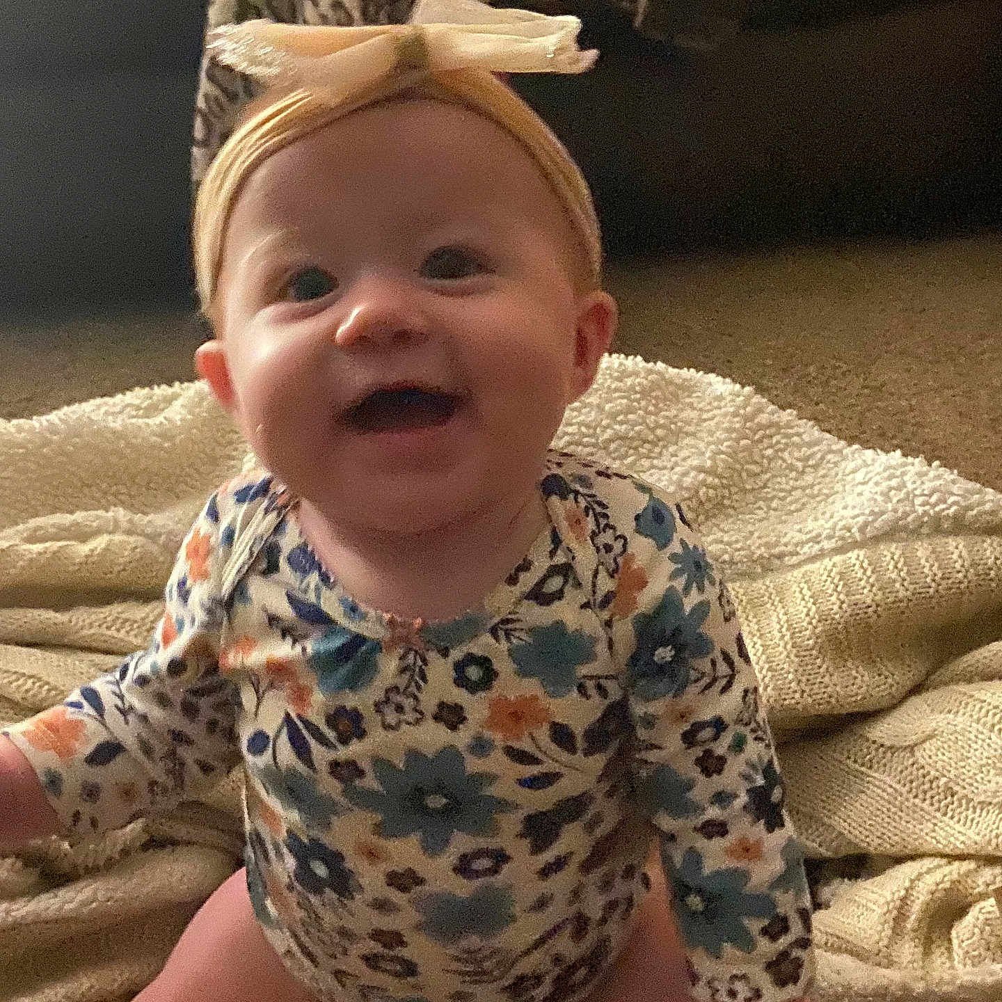 Amelia is registered to the contest to win money with this photo: baby, infant, child, portrait, smiling, happy, sitting, bow, headband, floral_clothing, onesie, blanket, couch, indoors, home, cozy, face, eyes, mouth, photography