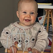 Léa participe au concours pour gagner de l'argent avec cette photo : baby, child, toy, wooden_toy, bead_maze, sweater, indoor, smiling, face, hands, furniture, backpack, papers, floor, person, cute, playing, happy, home, infant