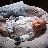 Noah is registered to the contest to win money with this photo: baby, infant, sleeping, blanket, baby_lounger, knitwear, mittens, white_clothing, soft_fabric, wooden_floor, cozy, indoors, child, portrait, peaceful, resting, newborn, comfort, cushion, warm