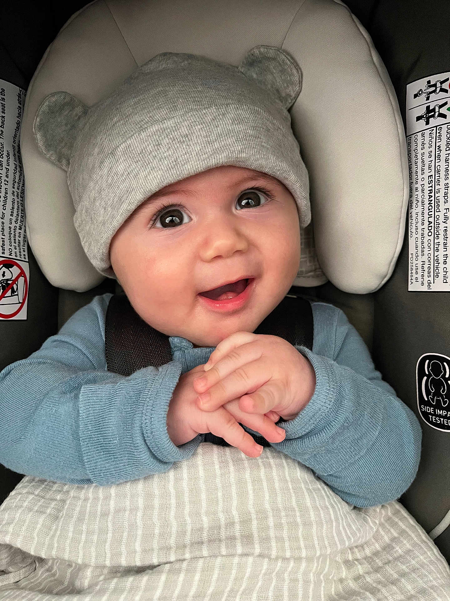 Kane joined the competition — help win amazing prizes! baby, child, infant, hat, bear_ears, blue_sweater, car_seat, blanket, smiling, happy, hands_clasped, cute, portrait, indoors, seatbelt, close_up, headwear, face, young_child, cozy