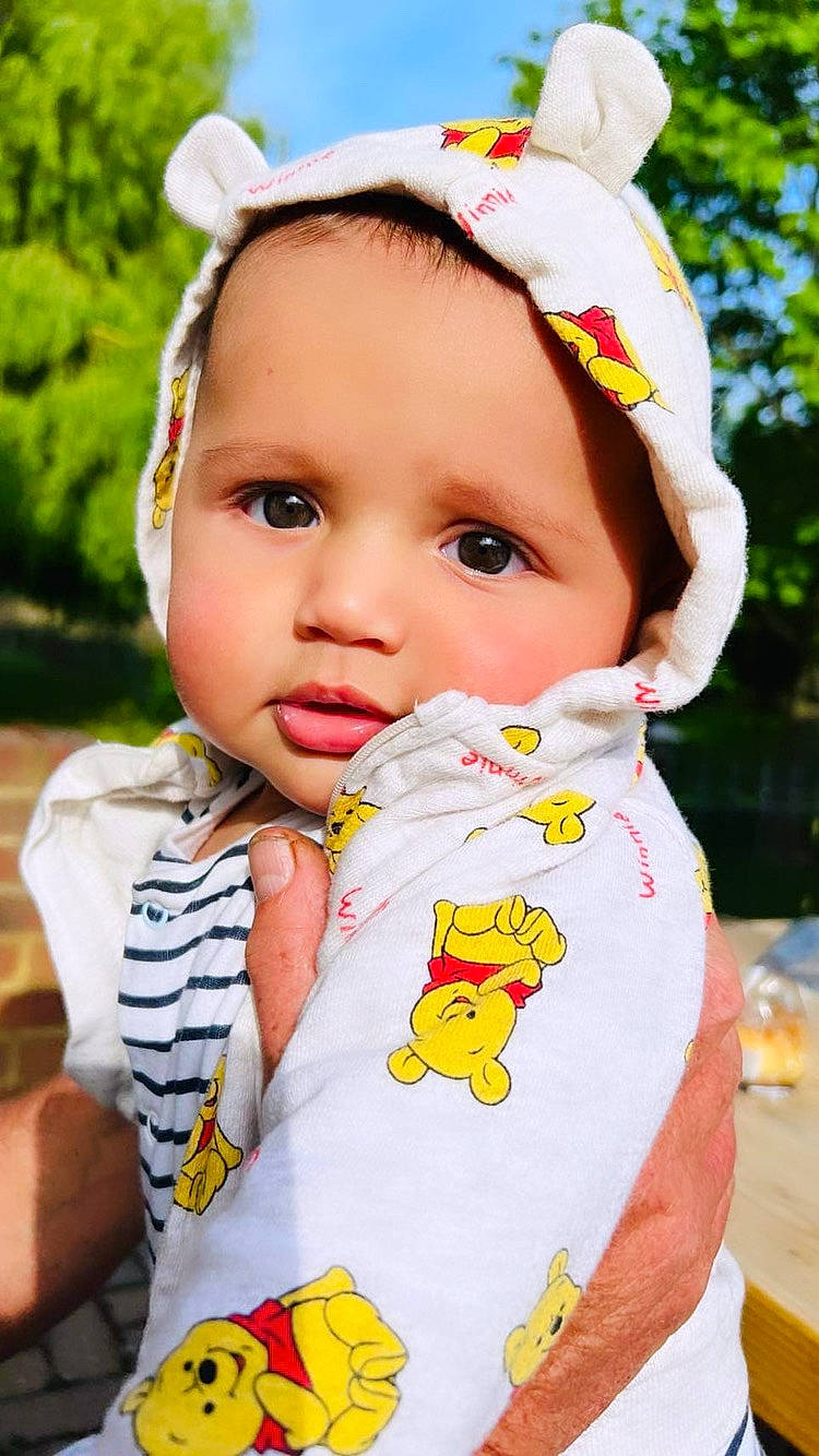 Benji is registered to the contest to win money with this photo: baby_toddler_clothing, bib, child, dress, eye, facial_expression, happy, hat, headwear, lip, organ, outerwear, person, pink, plant, product, skin, sleeve, textile, toddler