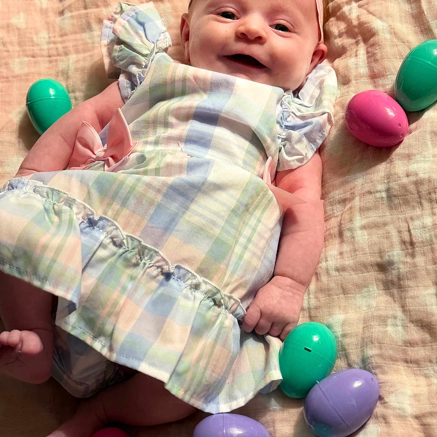 Anora is registered to the contest to win money with this photo: baby, infant, smile, dress, headband, flower, easter_eggs, plastic_eggs, blanket, pastel_colors, lying_down, happy, cute, child, indoors, soft_texture, colorful, celebration, holiday, portrait