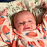 Anora is registered to the contest to win money with this photo: baby, infant, smiling, arms_up, strawberry_pattern, floral_quilt, clothing, cute, happy, face, head, skin, person, child, lying_down, portrait, closeup, indoors, soft_lighting, cozy
