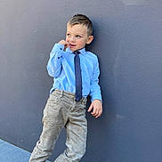 Liam participe au concours pour gagner de l'argent avec cette photo : child, boy, blue_shirt, tie, beige_pants, blue_shoes, playful, pose, smile, outdoor, gray_wall, side_view, casual, fashion, portrait, young, happy, person, concrete, footwear