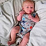 Cayden is registered to the contest to win money with this photo: baby, infant, newborn, onesie, sports_pattern, blanket, bedding, pillow, portrait, smile, legs, hands, toes, face, head, skin, indoor, cozy, decorative_wall, lying_down
