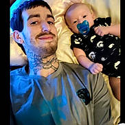 Cayden joined the competition — help win amazing prizes! adult, baby, bed, blanket, closeup, clothing, facial_hair, indoor, infant, lying_down, man, onesie, pacifier, parent, pillow, portrait, selfie, smiling, tattoo, together